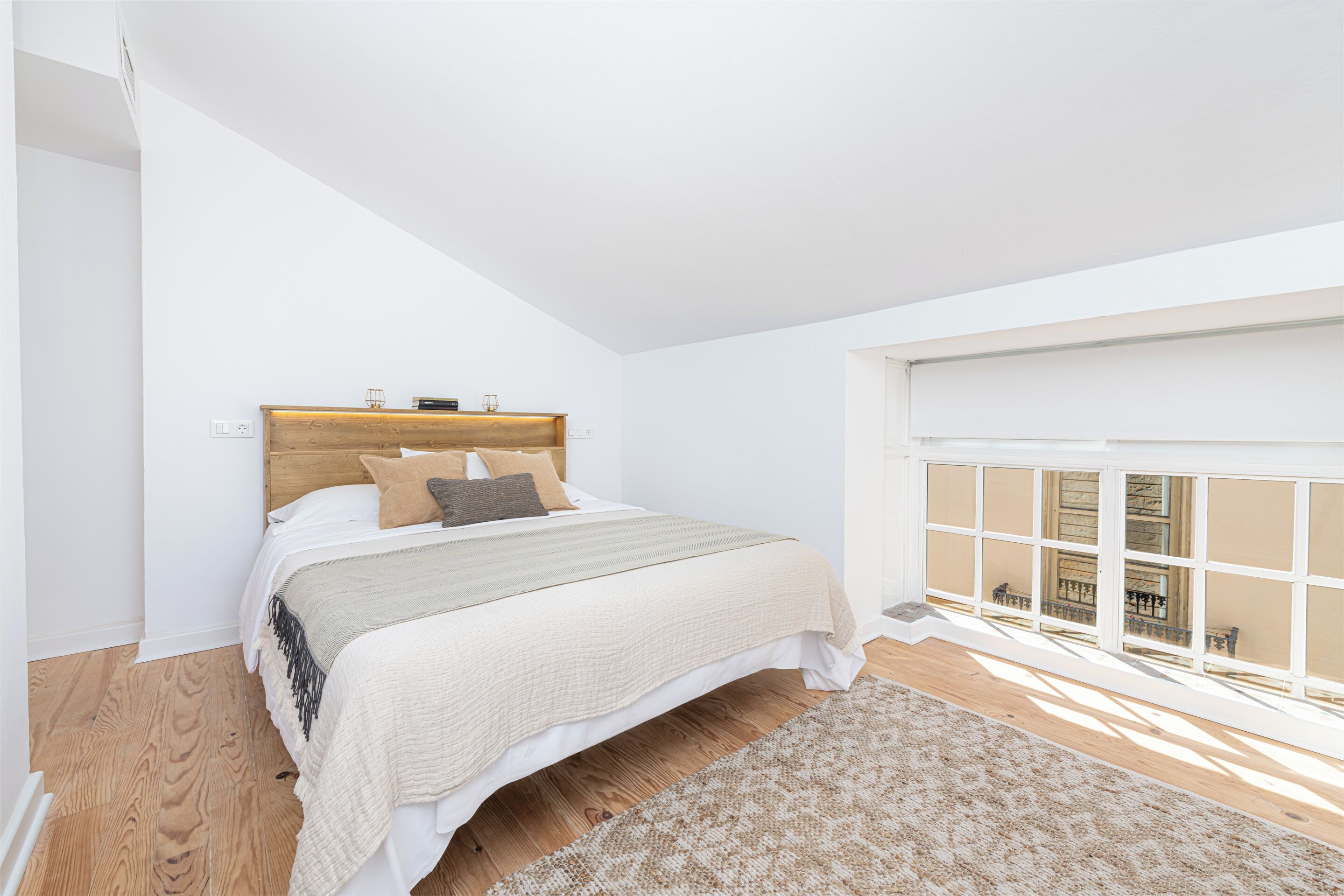 Une chambre à coucher avec un grand lit, une tête de lit en bois, une fenêtre donnant sur un beau paysage et un tapis à motifs.