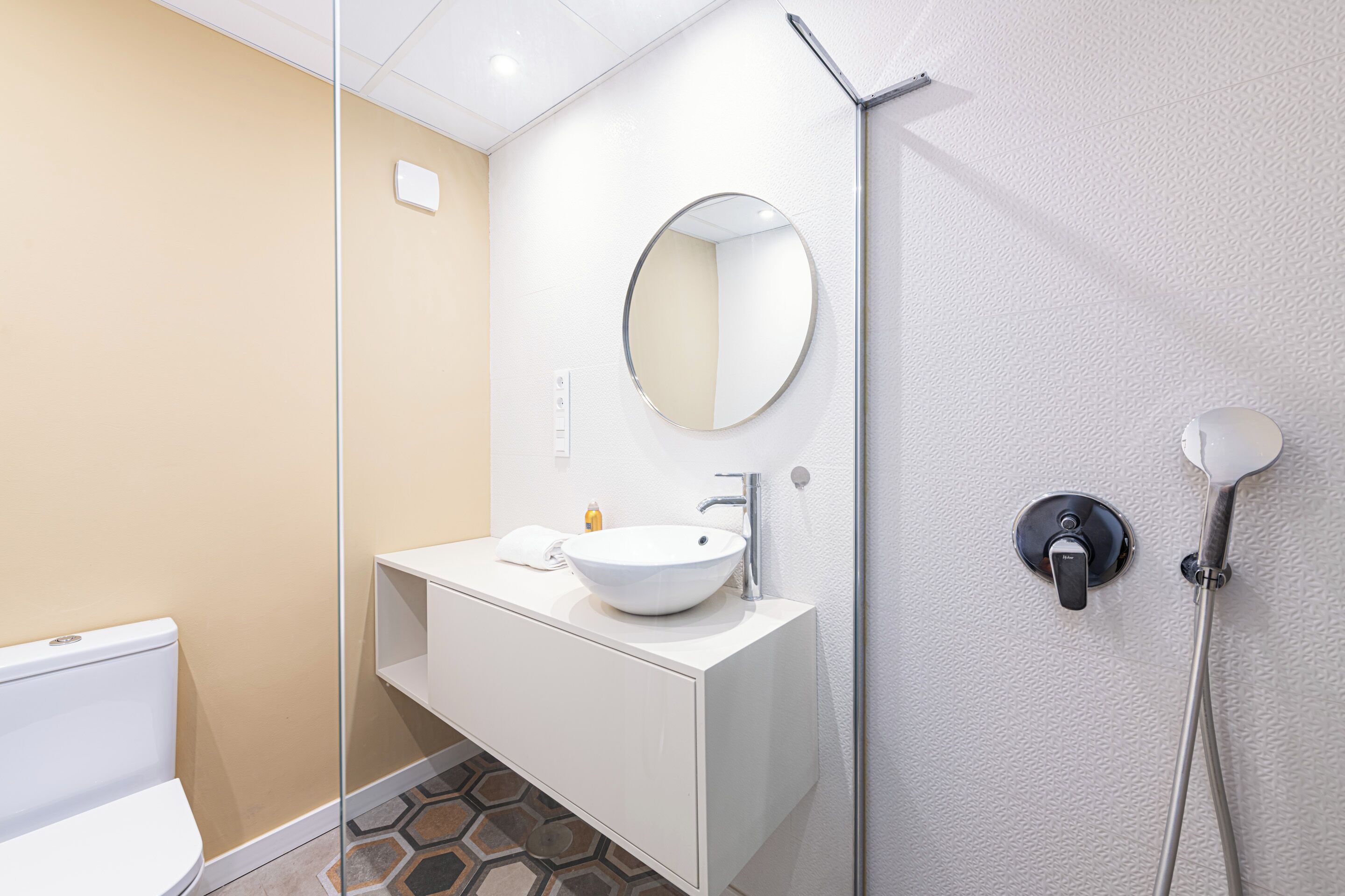 Een moderne badkamer met een wit wastafelmeubel, een ronde spiegel en een handdouche.