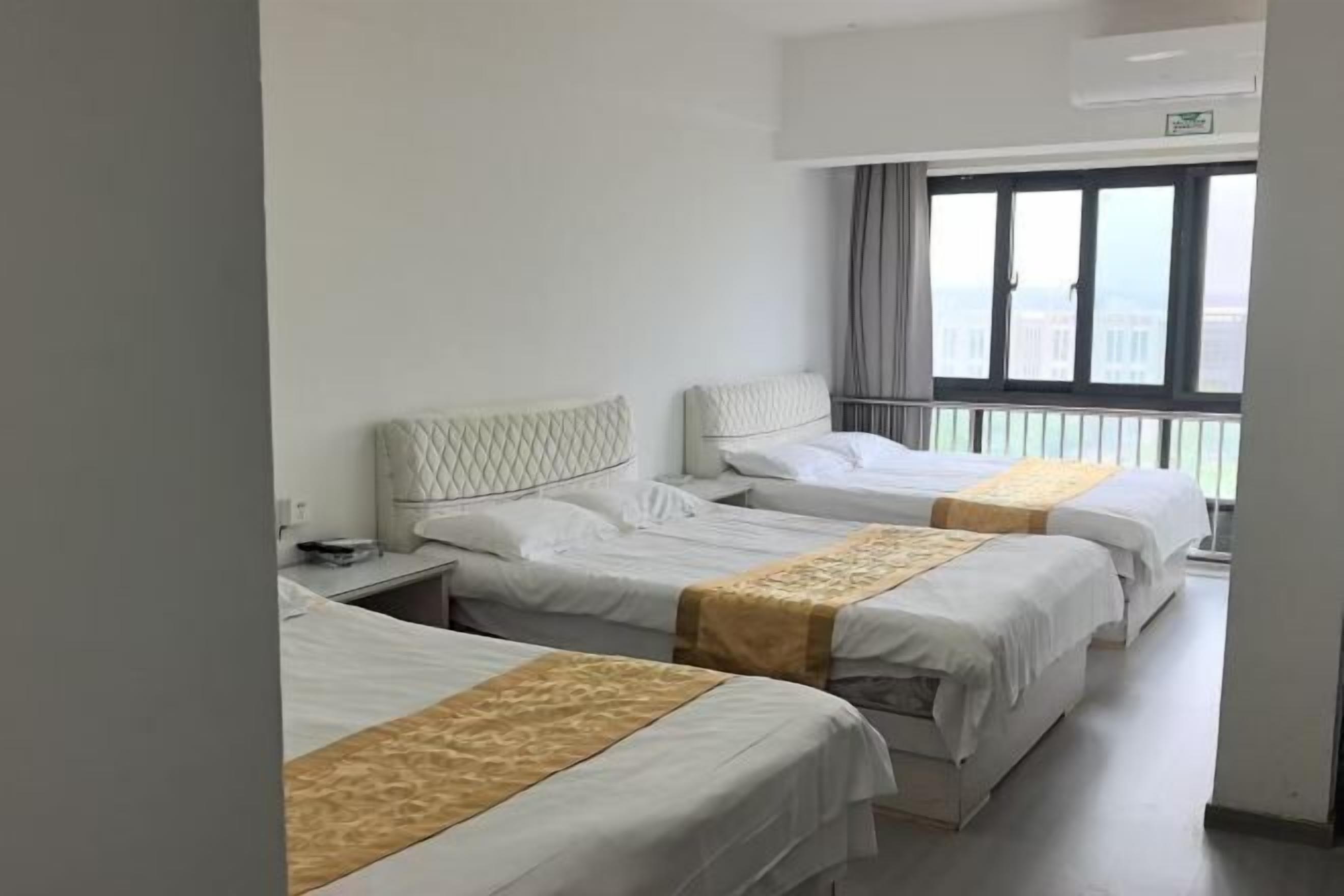 A hotel room with three beds, a window with a view, and a ceiling-mounted air conditioner.