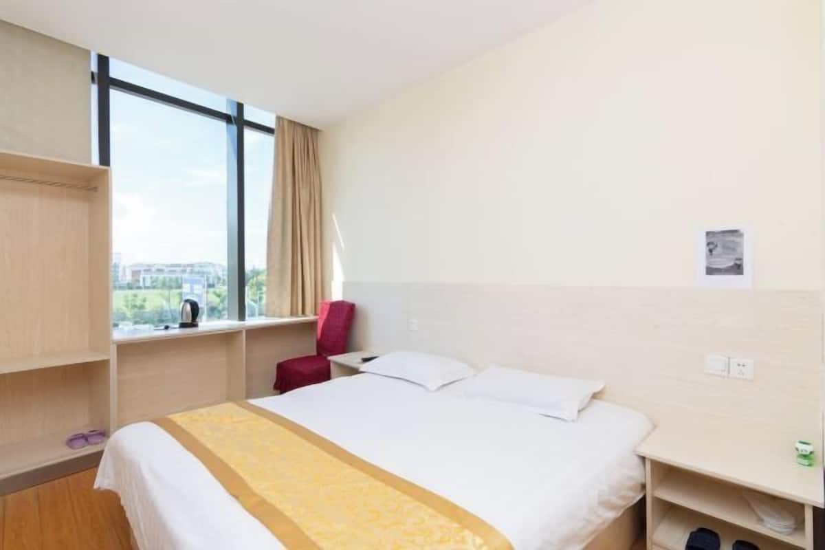 A hotel room with a bed, a window, a red chair, and a wooden shelf.