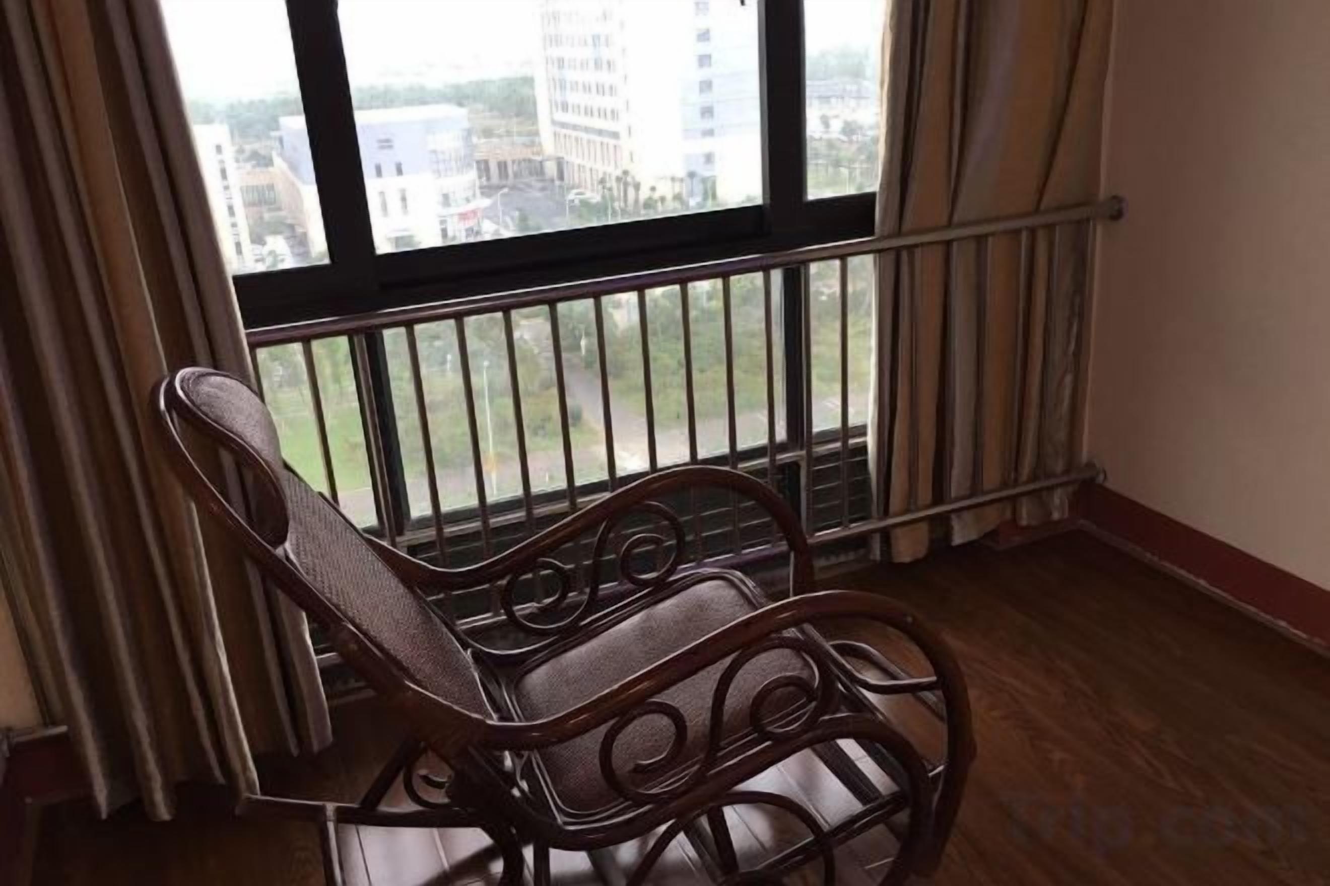 Un balcón con barandilla de metal, piso de madera y vista a edificios en la distancia.