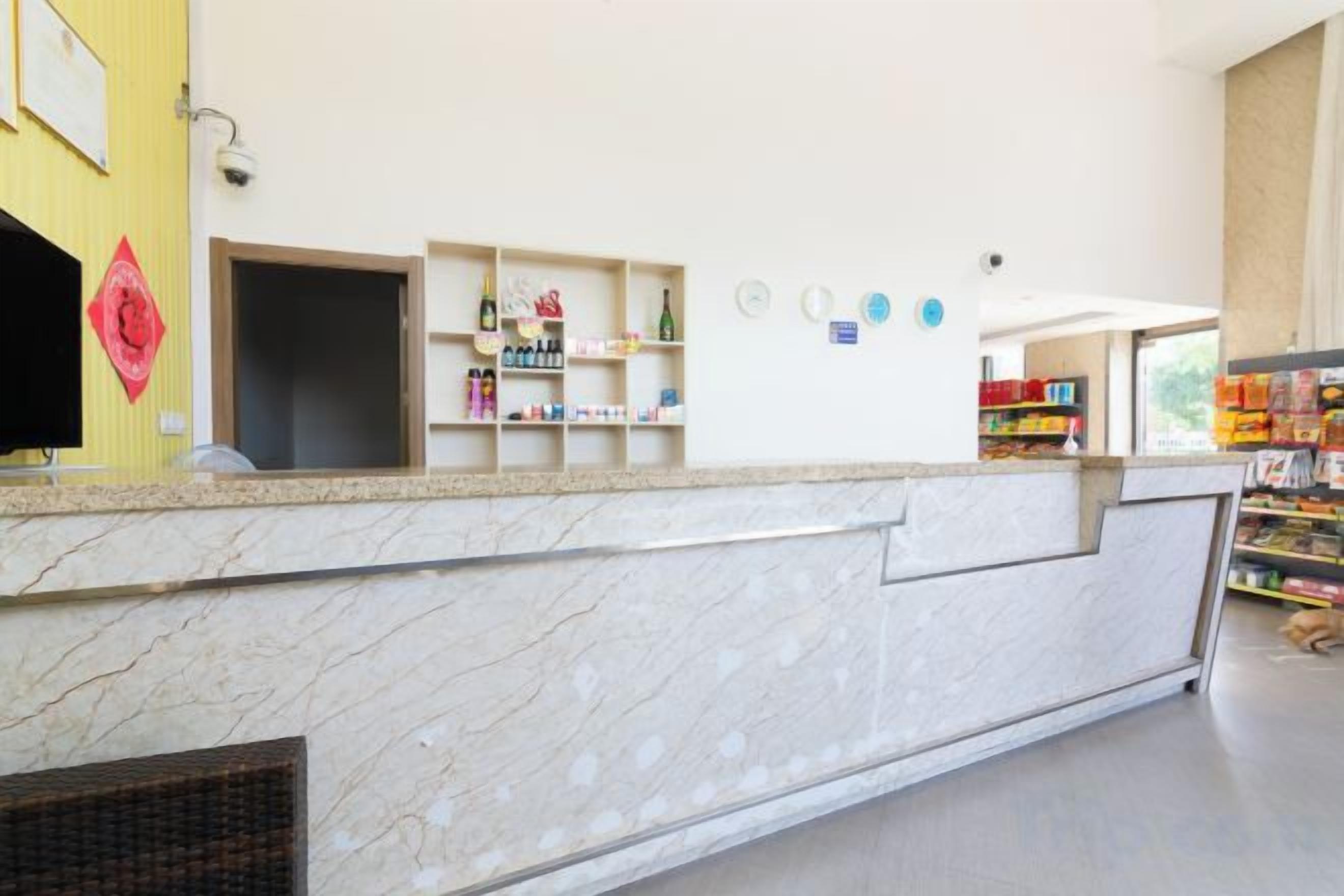 A hotel reception area with a marble counter, shelves with toiletries, and a view of the outside.