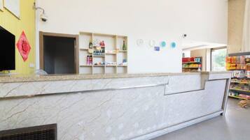 A hotel reception area with a marble counter, shelves with toiletries, and a view of the outside.
