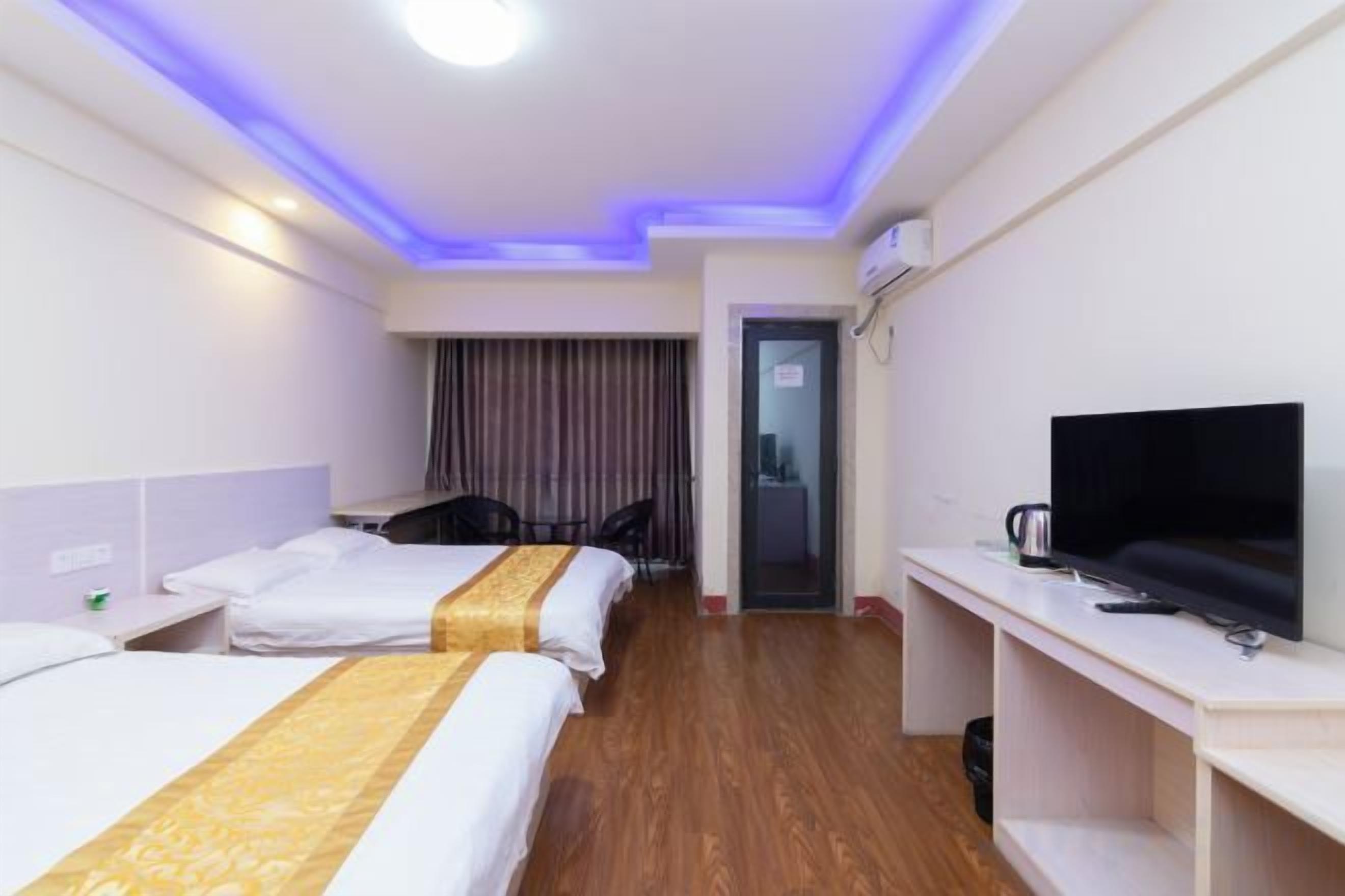 A hotel room with two beds, a desk, a chair, a television, and a minibar.