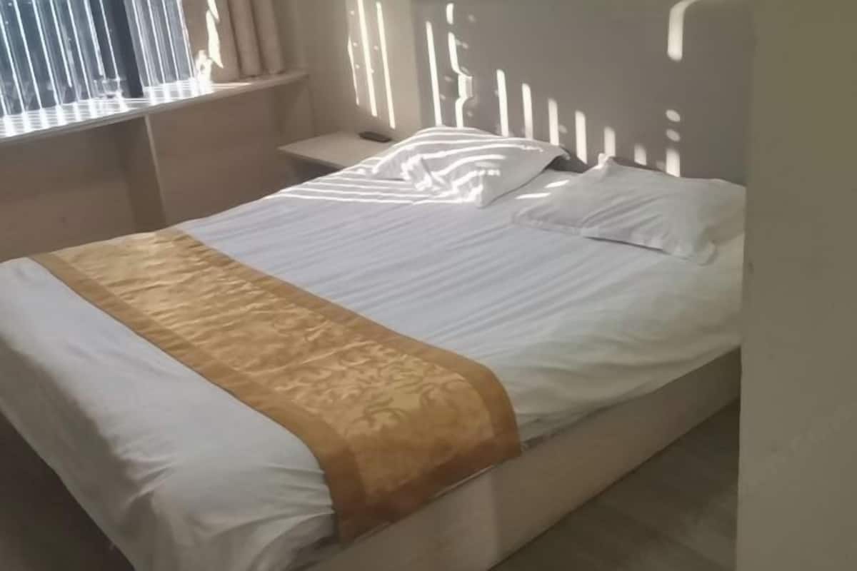 A bed with a white and gold bedspread, a nightstand, and a window with blinds.