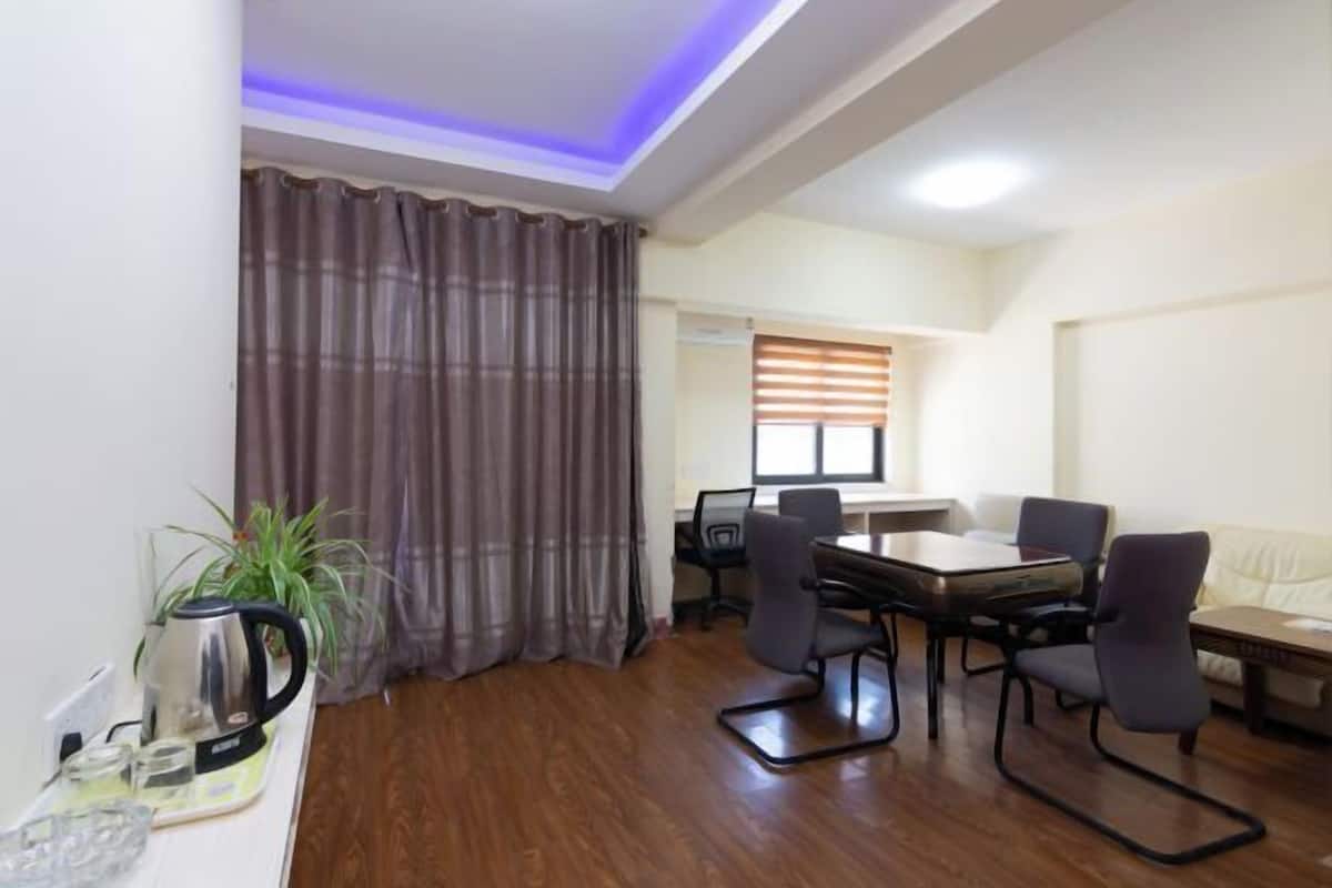 A room with a wooden floor, a dining table with four chairs, a sofa, a coffee table, a plant, and a kettle.