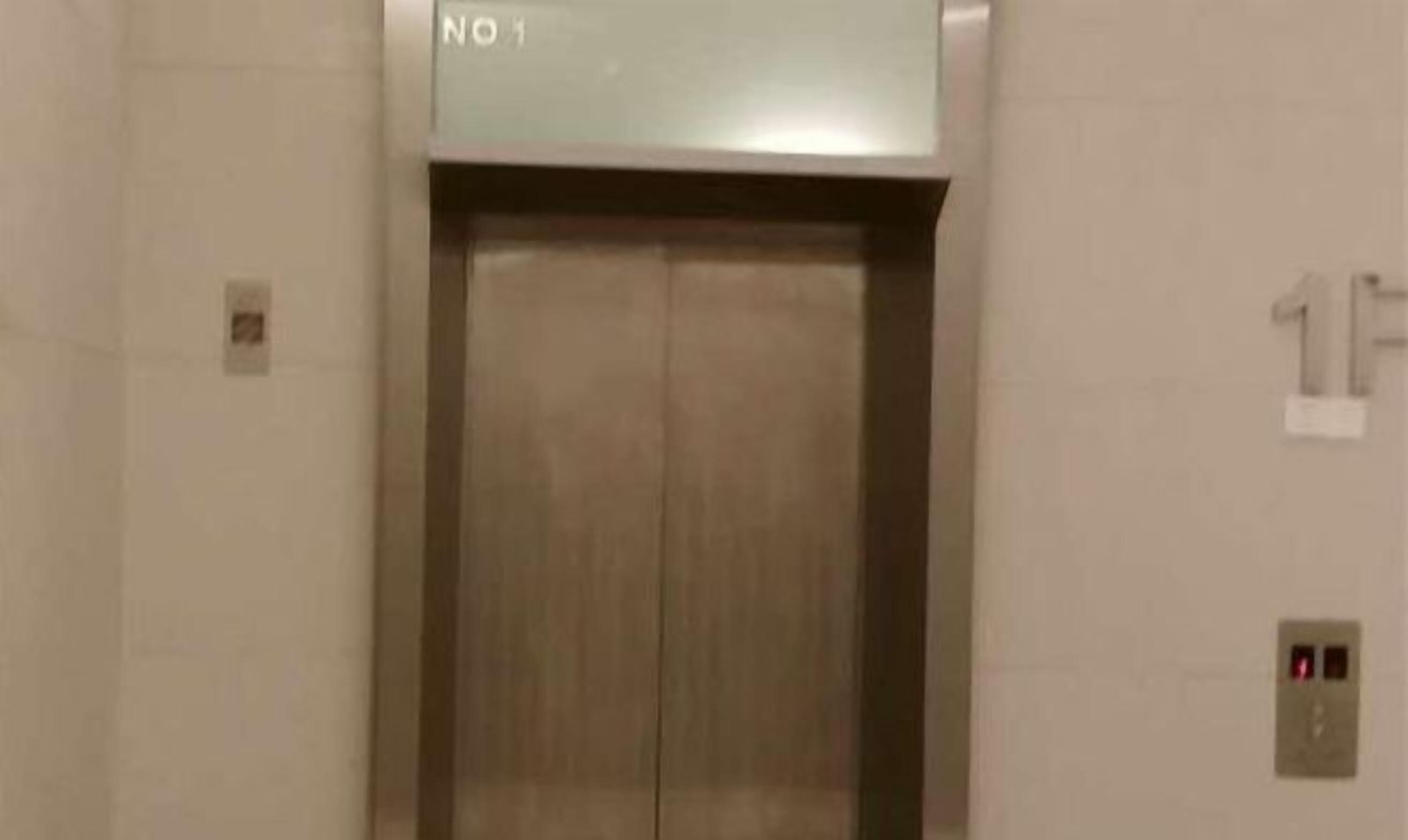 En elevator med metalfinish, en tydelig nødknap og et skilt på væggen, der angiver etagenummeret.