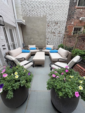 A patio with a sectional sofa, two side tables, and potted plants.