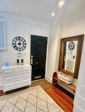 A hallway with a white dresser, a black door, a mirror, and a patterned rug.