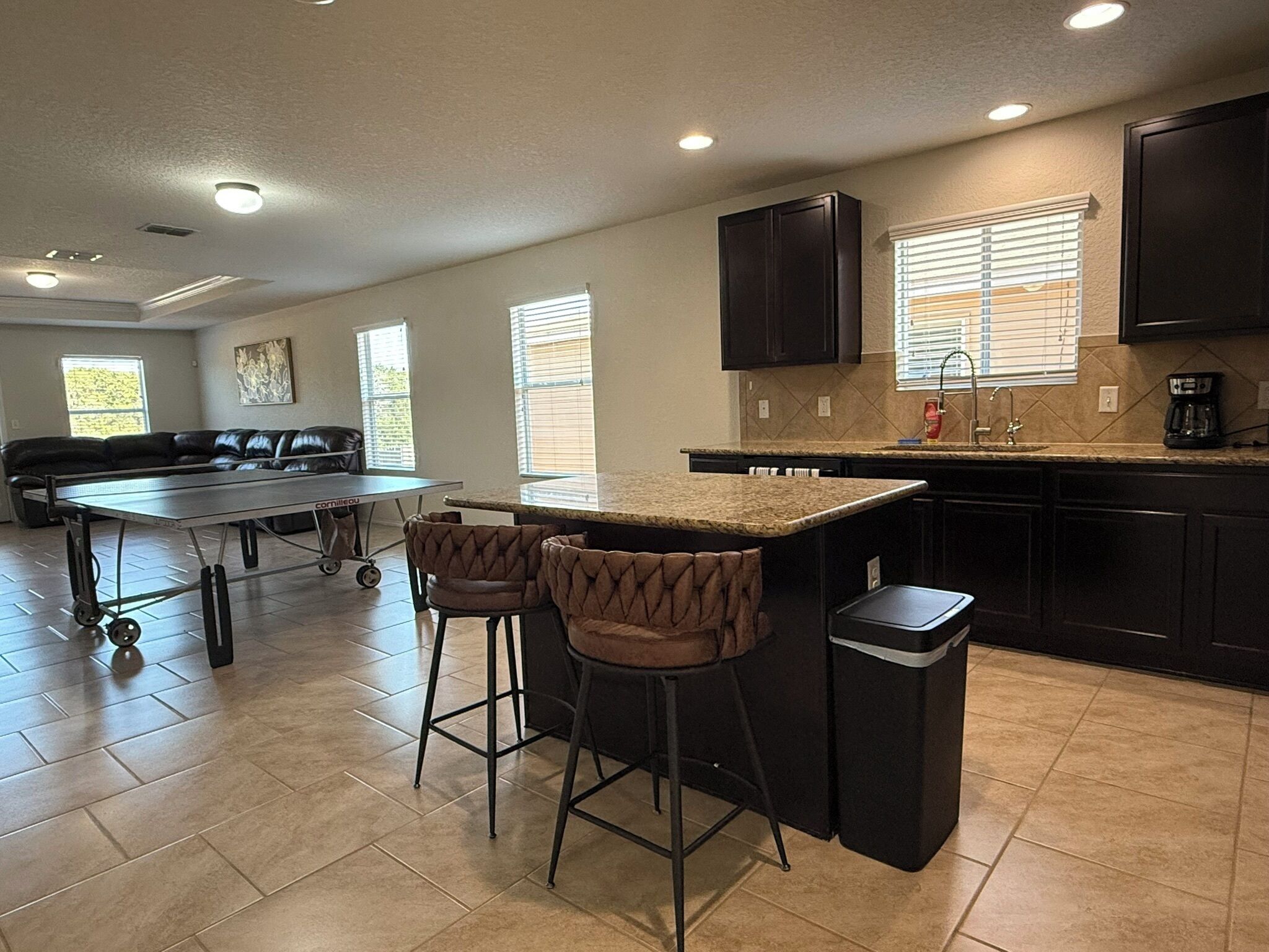 A modern kitchen with dark cabinetry, a marble countertop, and a bar area with stools.