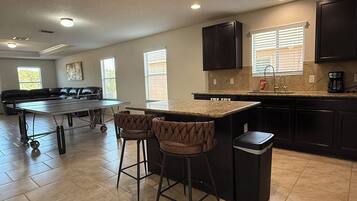 A modern kitchen with dark cabinetry, a marble countertop, and a bar area with stools.