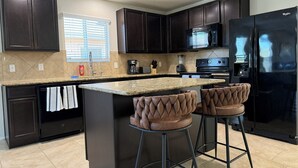 A modern kitchen with dark cabinets, a granite countertop, a black refrigerator, and two bar stools.