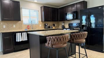 A modern kitchen with dark cabinets, a granite countertop, a black refrigerator, and two bar stools.