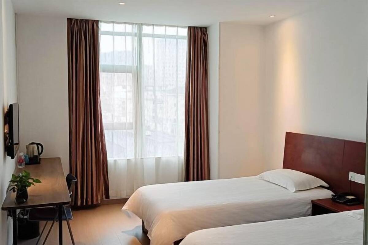 A hotel room with two beds, a desk with a chair, a TV, and a window with curtains.