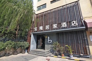 A hotel entrance with a modern facade, a visible entrance door, and potted plants in front. - Baolong Homelike Hotel (Shanghai Xuhui) (Shanghai)