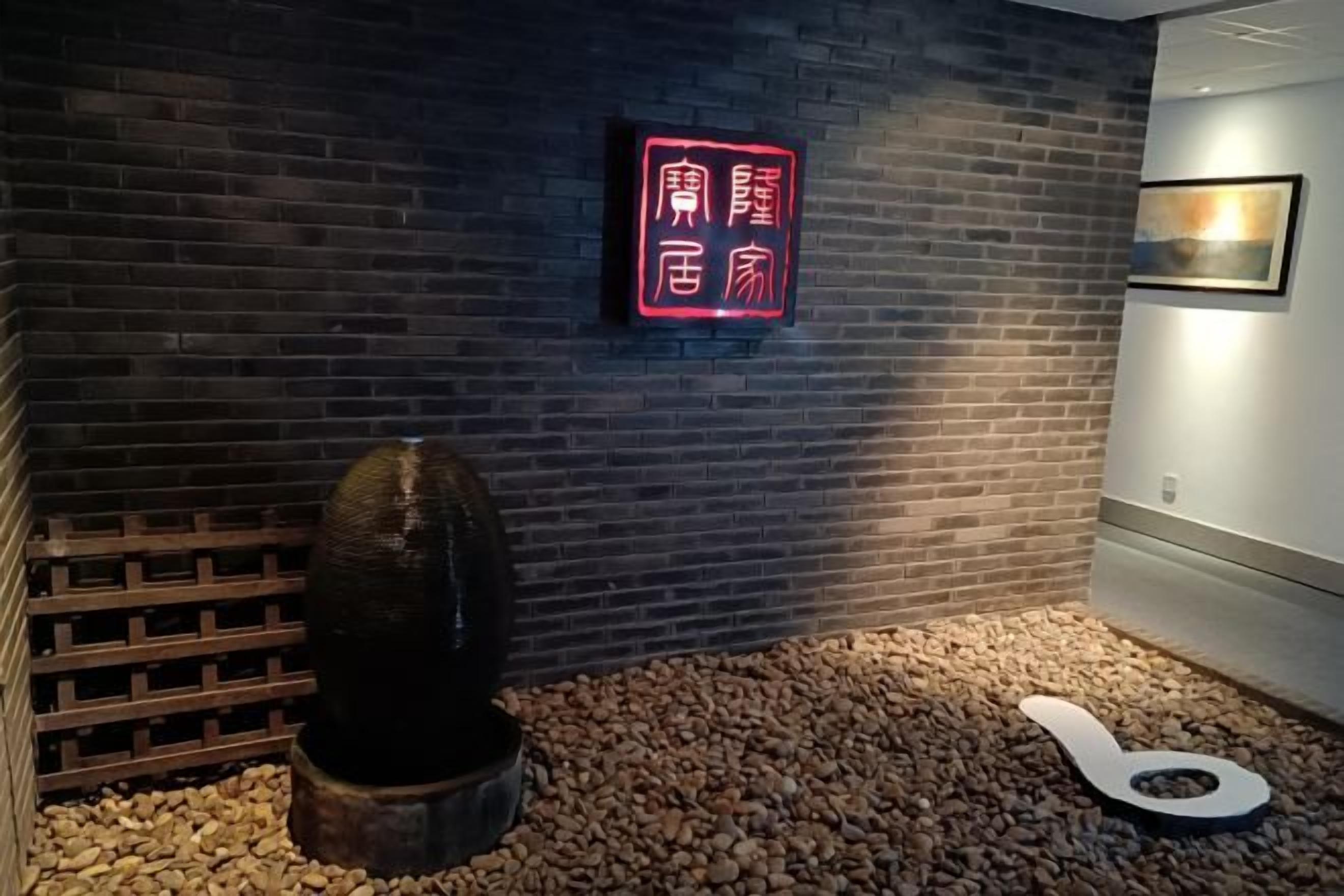 A room with a brick wall, a neon sign, a wooden lattice, and a textured sculpture.
