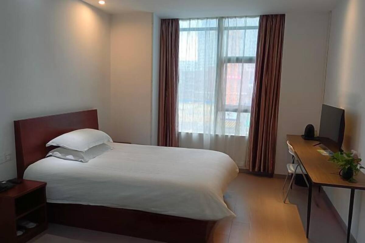 A hotel room with a bed, a desk, a chair, a TV, and a window with curtains.