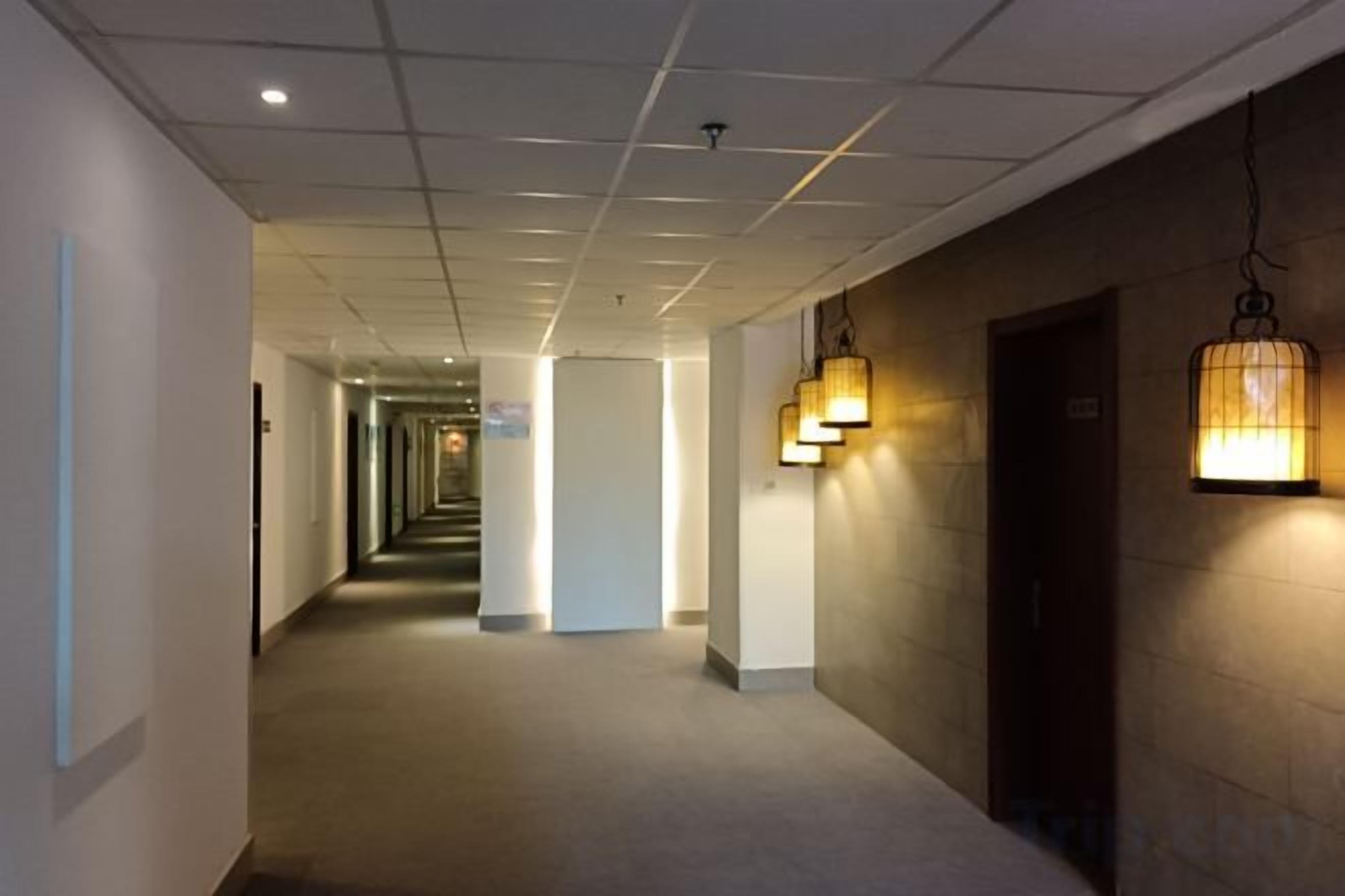 A hotel corridor with a long hallway, doors on the right, and a light fixture on the wall.