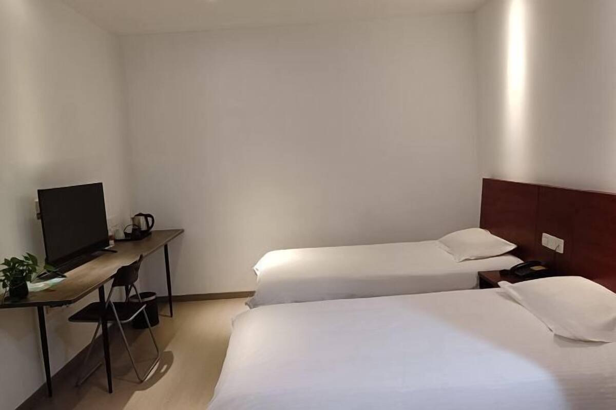 A hotel room with two single beds, a desk with a television, and a small table with a plant.