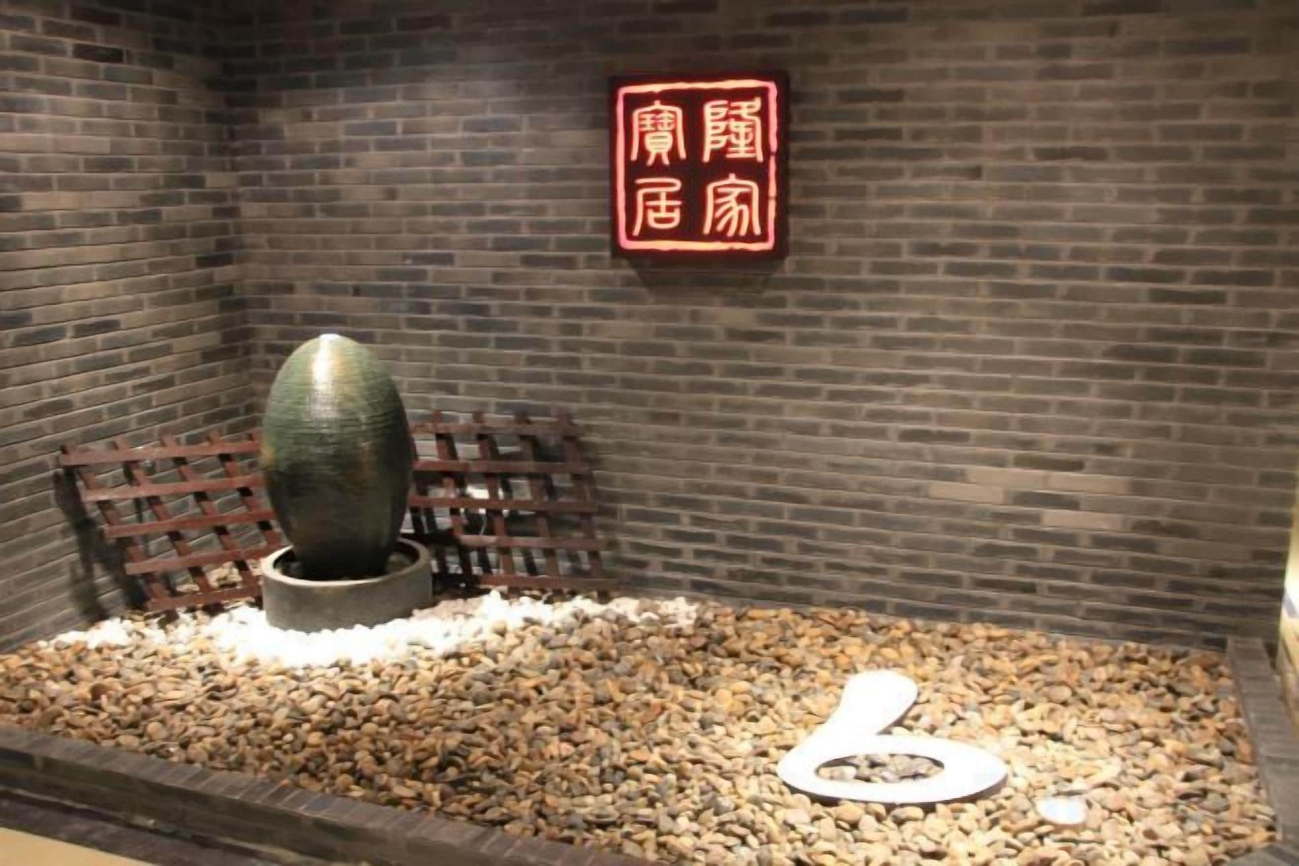 Een kamer met een bakstenen muur, een houten bank, een stenen beeldhouwwerk en een bord met Chinese karakters.