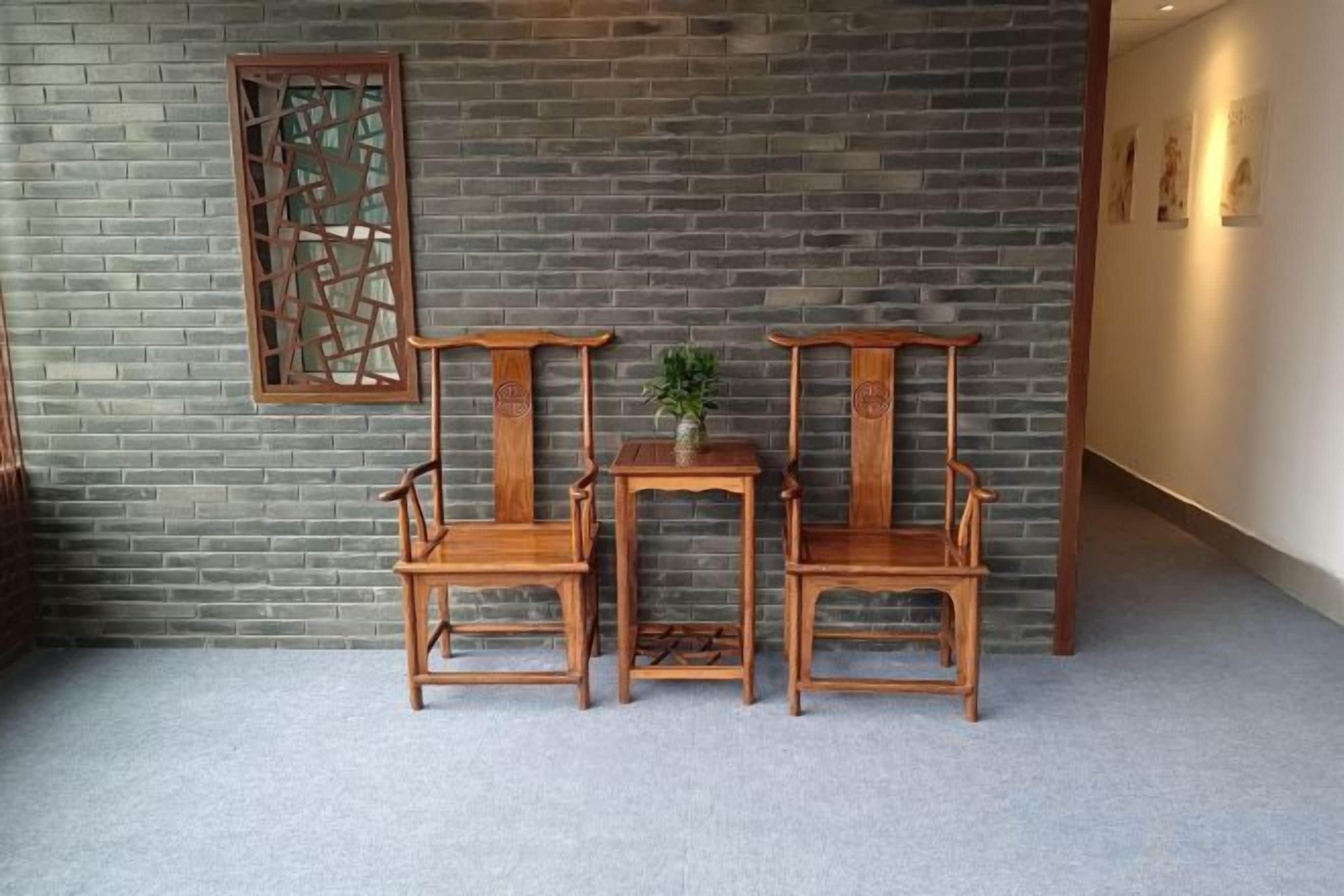 A room with a brick wall, two wooden chairs, a small table, and a decorative screen.