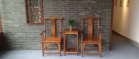 A room with a brick wall, two wooden chairs, a small table, and a decorative screen.