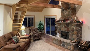 Een gezellige woonkamer met een stenen openhaard, een houten trap en een kerstboom.