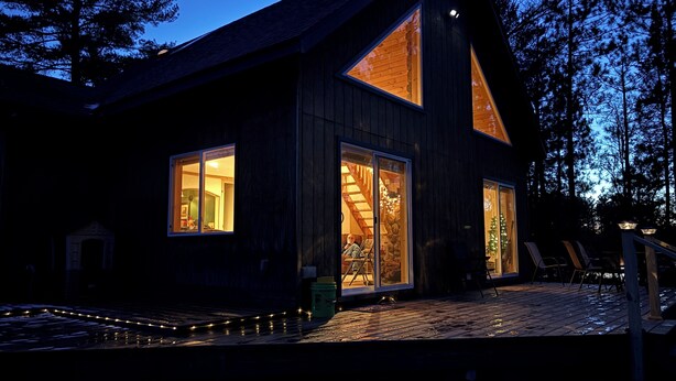 Een houten chalet met grote ramen, een terras en een kerstboom.