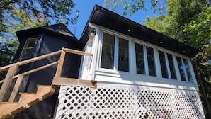 A cabin with a wooden staircase leading to a deck, surrounded by trees.