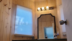 A wooden-paneled room with a kitchen area, including cabinets, a window with blinds, a mirror, and a ceiling light fixture.