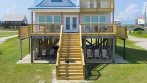 A two-story beachfront house with a wooden deck, a staircase, and a covered seating area. - Waterfront ~ Ohana  ~ Sleeps 10 (Dauphin Island)