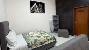 Une chambre moderne avec un lit, un canapé gris, une porte en bois et un mur noir orné d’un tableau encadré.