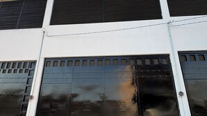 Un bâtiment moderne à la façade blanche, doté de grandes portes de garage noires et d’un toit métallique muni de grilles de ventilation.