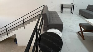 Un salon moderne avec un escalier, un canapé gris, une table ronde noire et un téléviseur à écran plat fixé au mur.