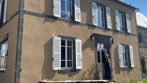 A two-story building with white shutters, a stone foundation, and a clear blue sky. - "L'Hôtel d'O', a former coaching inn in a typical Cantal village. (Neuvéglise-sur-Truyère)