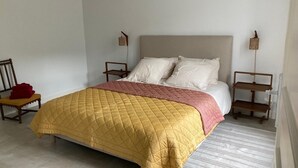 A bed with a quilted yellow and pink bedspread, two white pillows, and wooden nightstands with small lamps. - "L'Hôtel d'O', a former coaching inn in a typical Cantal village. (Neuvéglise-sur-Truyère)