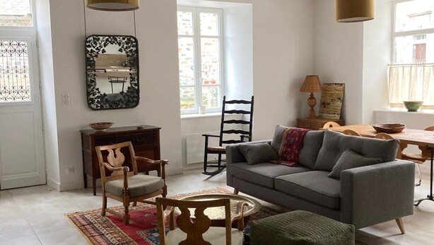 A living room with a grey sofa, wooden chairs, a patterned rug, and a wooden ceiling with exposed beams. - "L'Hôtel d'O', a former coaching inn in a typical Cantal village. (Neuvéglise-sur-Truyère)