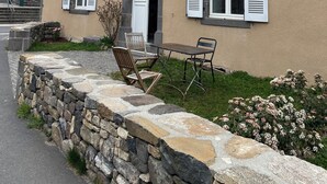 A two-story building with white shutters, a stone staircase, and a stone wall with a bench and chairs. - "L'Hôtel d'O', a former coaching inn in a typical Cantal village. (Neuvéglise-sur-Truyère)