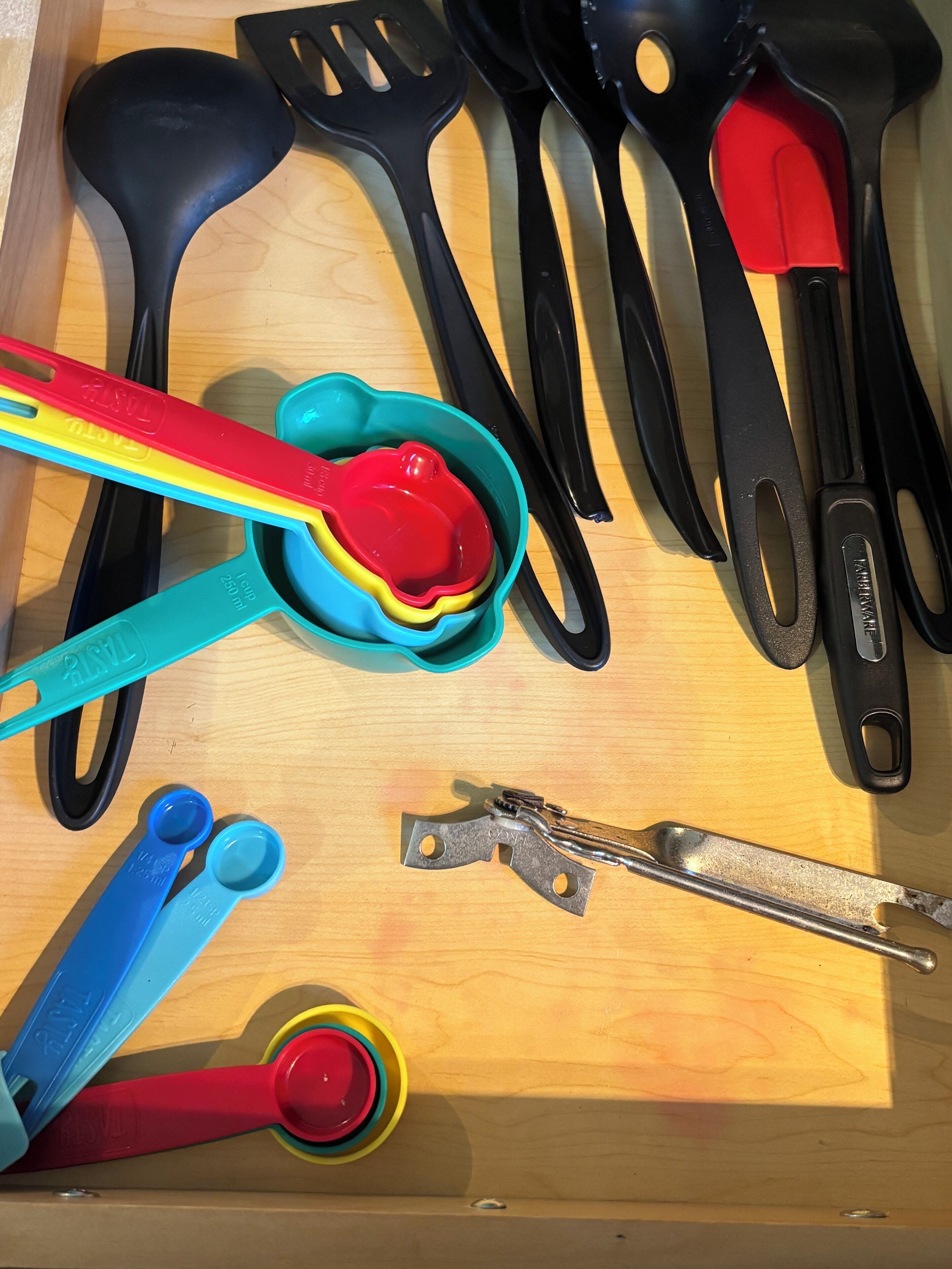 A drawer containing various kitchen utensils including spatulas, tongs, and measuring cups.