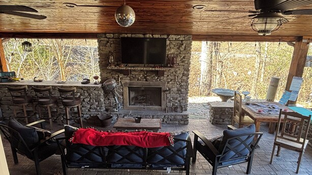 Un espacio de estar al aire libre cubierto con paredes de piedra, una chimenea y una barra.