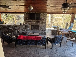 A covered outdoor seating area with stone walls, a fireplace, and a bar counter. - The Cedar Cabin at Center Hill Lake (Smithville)