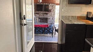 Una cocina con chimenea de piedra, un comedor con mobiliario exterior y un televisor grande montado sobre la encimera.