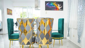 A dining area with a modern table and chairs, a green sofa, and a painting on the wall.