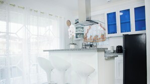 A modern kitchen with white bar stools, a black refrigerator, and blue cabinets.