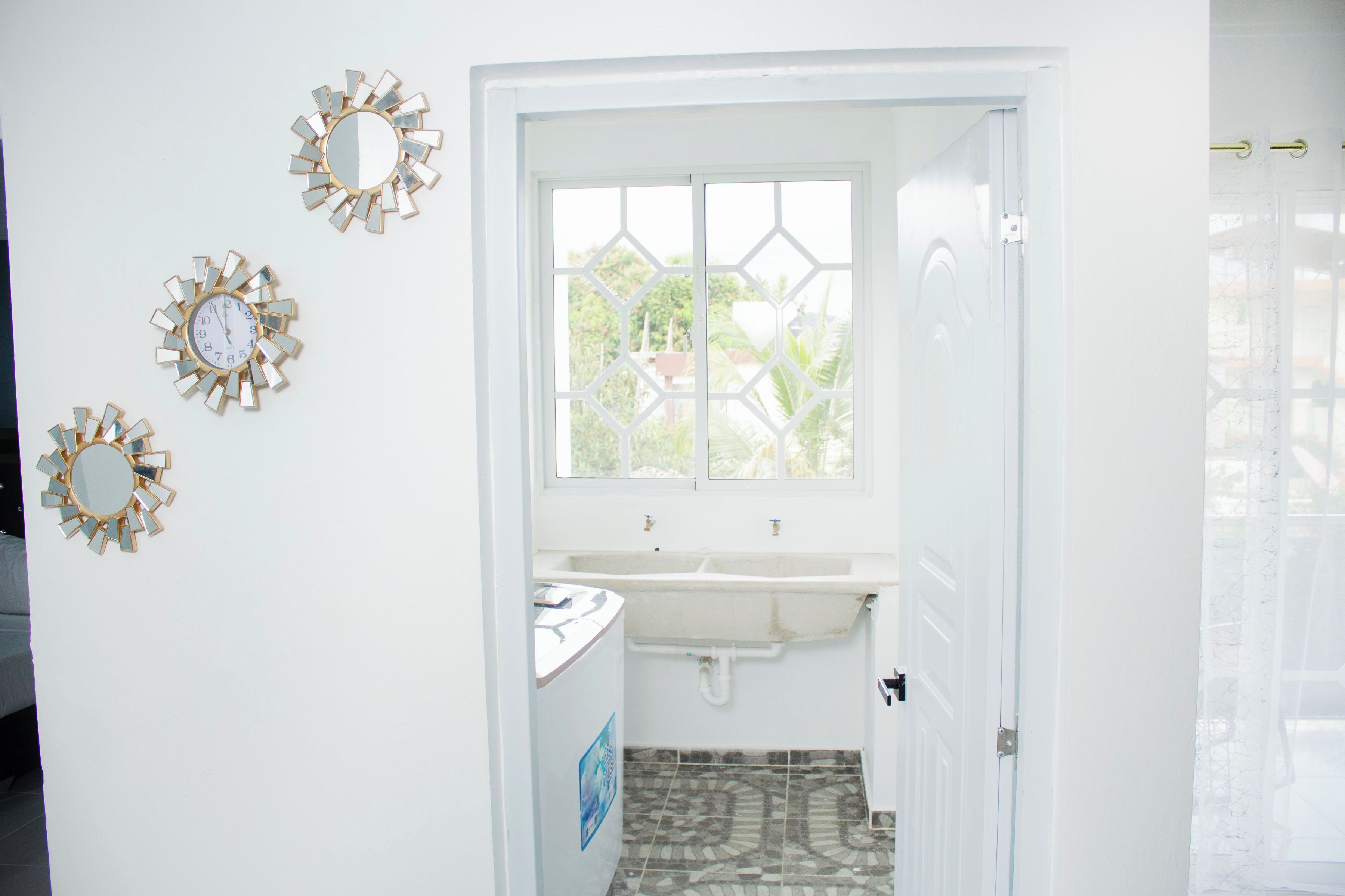 A bathroom with a white sink, two mirrors, and a window with a geometric pattern.