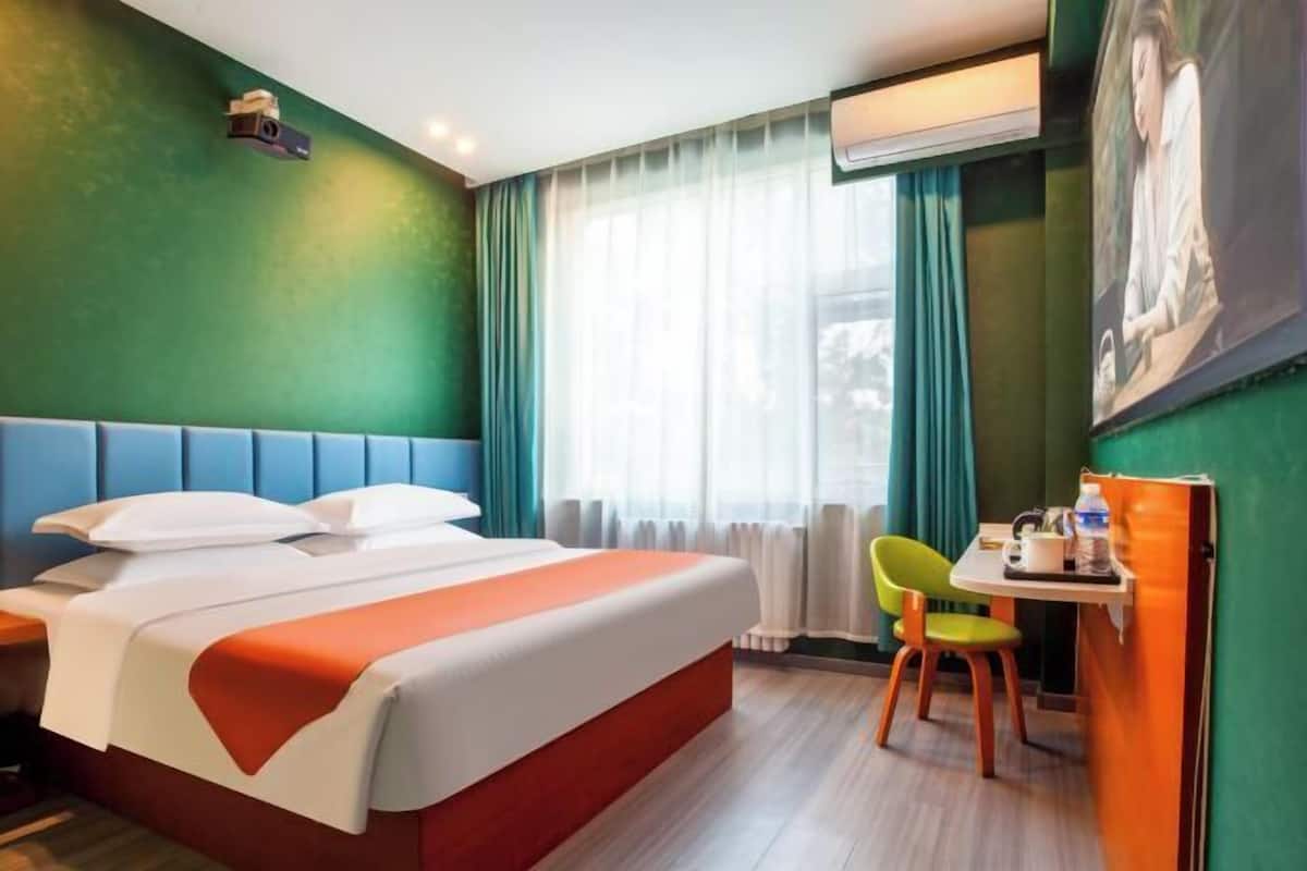 Ett hotellrum med en säng, ett skrivbord, en stol och ett fönster med gardiner.