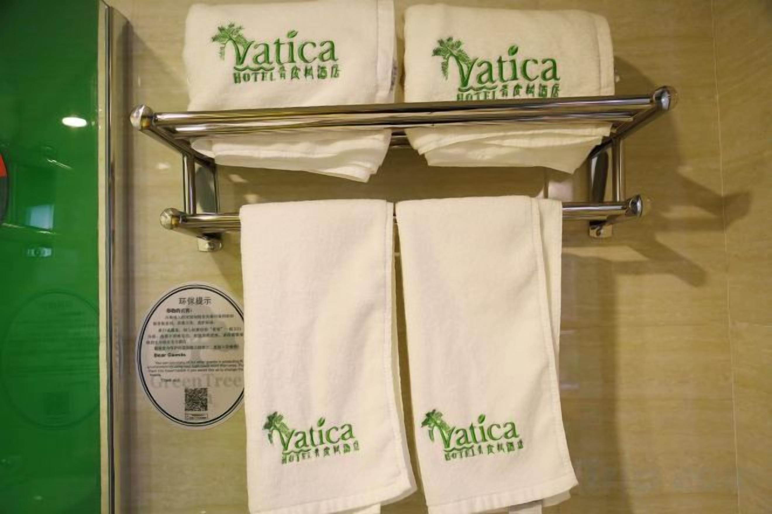 Un baño con dos toallas blancas colgadas en un perchero metálico, cada una con el logo 'Vatica'.