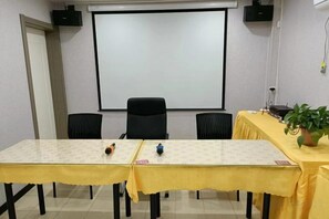 A conference room with a projector screen, two tables with yellow tablecloths, black chairs, and a potted plant. - Shell Hotel (Chaoyang shoe city store, Chaoyang Street, Taiyuan) (Taiyuan)