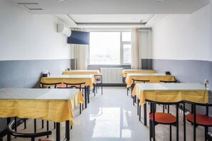 Une salle de classe avec des tables et des chaises, une fenêtre avec des rideaux et un radiateur.