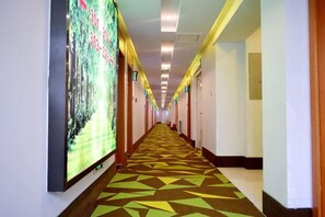 A long hallway with a patterned carpet, doors on both sides, and a large digital screen on the left. - Shell Hotel (Chaoyang shoe city store, Chaoyang Street, Taiyuan) (Taiyuan)